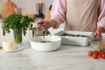 Woman making spinach lasagna at marble table in kitchen, closeup