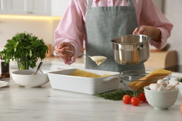 Woman spreading bechamel sauce onto spinach lasagna at marble table indoors, closeup