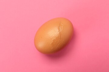 One egg with cracked shell on pink background, top view