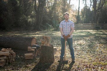 Country homesteading man with ax cutting firewood for campfire or stove in field