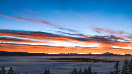 Vivid orange sunrise over dense cloud inversion covering much of Fraser Valley, BC, with alpine...