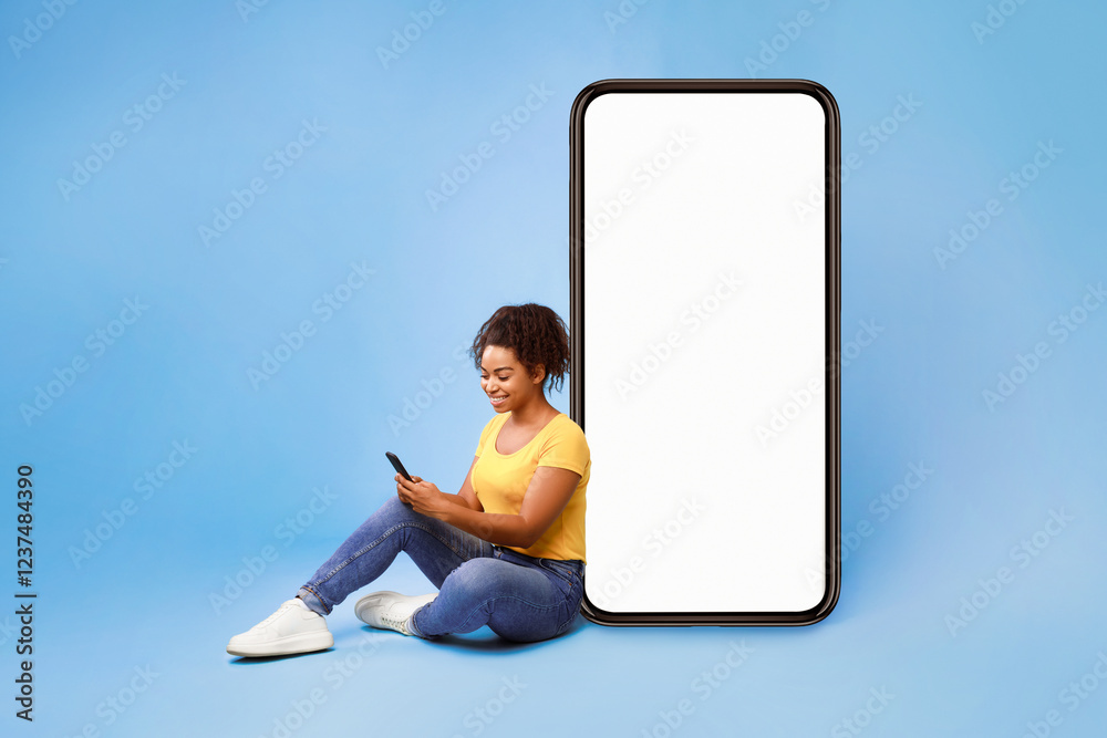 Poster cheery african american lady sitting near big cellphone with empty white screen, using mobile device