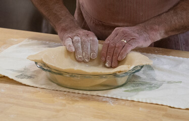 On a wooden kitchen worktop an unrecognizable adult male fits a raw pie shell into a glass dish.