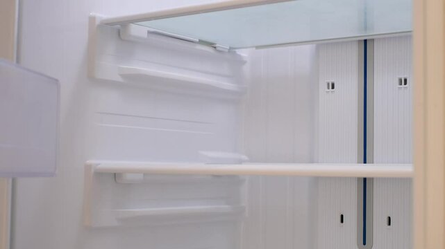 Modern white open refrigerator close-up with empty shelves.