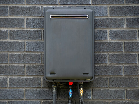 Black Outdoor Tankless Gas Water Heater Installed at Dark Brick Wall