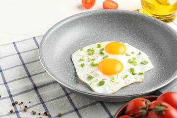 Tasty fried eggs with green onion in frying pan on table, closeup