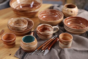 Different beautiful pottery and set of clay crafting tools on wooden table, closeup