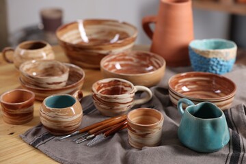 Different beautiful pottery and set of clay crafting tools on wooden table indoors, closeup