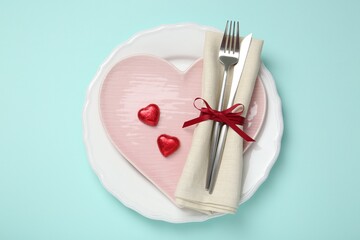 Romantic place setting with cutlery and plates on light blue background, top view. Valentine's day celebration