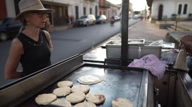 A tourist observes the preparation of delicious pupusas and quesillo at a street food vendor in Granada, Nicaragua, enjoying the local culinary experience.