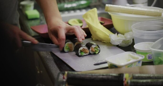 Home sushi chef precisely slicing maki rolls in his kitchen using a razor sharp Japanese knife, shallow dof, crabbing shot