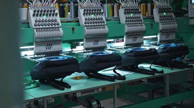Embroidery machine stitching detailed patterns on fabric in a manufacturing setting, multi unit in warehouse, static