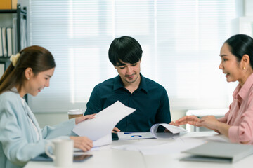 Three professionals collaborate and discuss documents in a bright office setting, showcasing teamwork and communication.