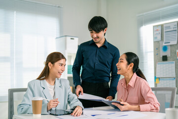 A group of three professionals collaborate in a bright office, discussing documents and sharing ideas, showcasing teamwork and engagement.