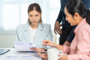 Obraz premium Two women collaborate at a table, reviewing documents, while a man stands nearby, suggesting teamwork and business discussions.