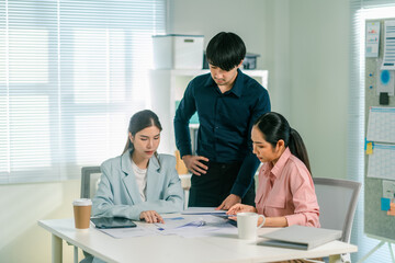 Fototapeta premium A team of three professionals collaborates on a project, focusing on documents laid out on a table in a bright office space.