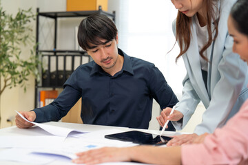A team collaborates at a table, reviewing documents and using a tablet for discussion and planning in a modern workspace.