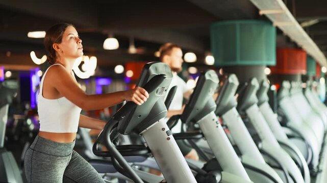 Young athletic woman in sportswear training on elliptical machine in gym