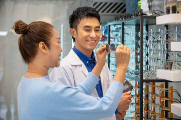 Asian male optician assisting senior female customer in choosing sunglasses in eyewear store