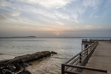 Obraz premium Dakar, Senegal – Sunrise over the Atlantic Ocean, seen from a wooden pier in Ouakam, a district municipality in the city of Dakar. The calm waters and soft morning light create a serene coastal landsc