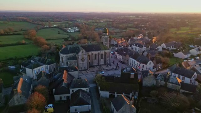 Eglise Saint-Gervais et Saint-Protais, church, Jublains town at sunset, Mayenne in France. Aerial drone backward tilt-up reveal