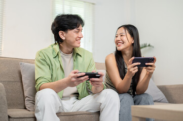 A lovely Asian couple enjoying playing a mobile game on their smartphones.