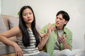 A toxic relationship in a young couple. An unhappy Asian couple sits in the living room, arguing.