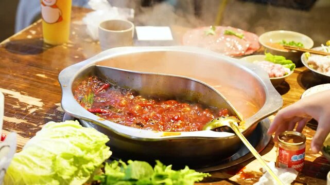 Slow-motion close-up of a traditional Chongqing Sichuan hotpot in a restaurant, showcasing bubbling spicy broth, fresh ingredients, and the vibrant dining experience of Chinese cuisine.