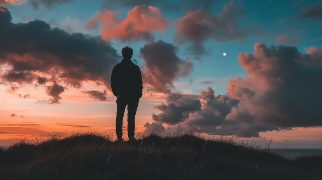 Silhouette of a man standing on a hilltop overlooking a dramatic sunset sky with clouds and a star.