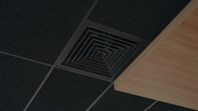 A low angle shot of a modern black HVAC vent blowing cold air. The vent is set in a dark acoustic drop ceiling tile grid next to a light wooden ceiling panel, cooling, airflow, ventilation,