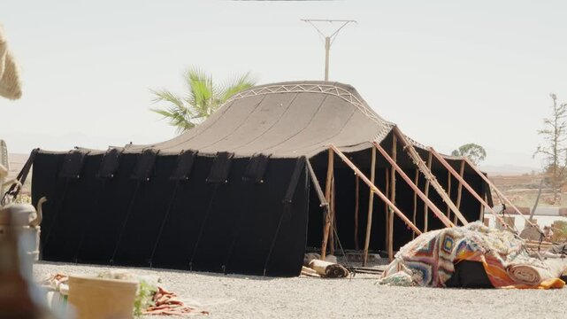 A traditional Berber tent stands tall against the clear Moroccan sky. Its black canvas and wooden frame hint at a nomadic lifestyle, promising a journey into cultural experiences.