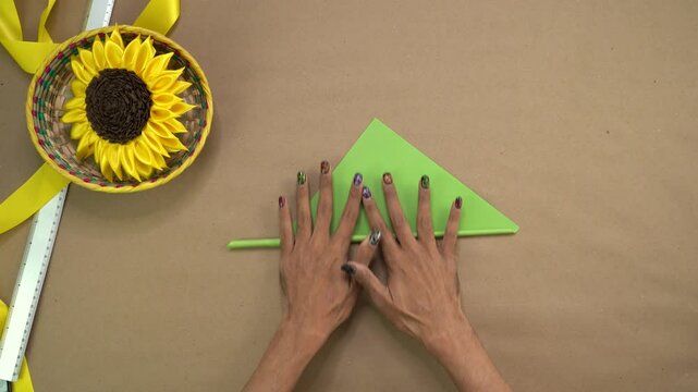 Artist's fingers deftly roll piece of green paper, carefully crafting delicate ribbon sunflower