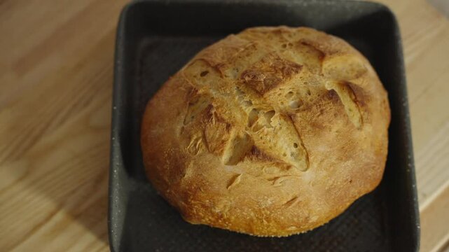 Looking down from overhead at a loaf of resh baked bread being placed on a counter top to cool.