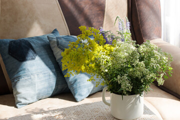 Interior. Room. Bouquet of white, field flowers in iron, rough. a white mug on a table covered with a lace tablecloth. Sofa, pillows from old jeans. Summer. Cosiness. Rustic. Country house.