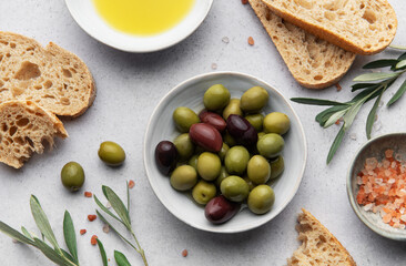 Green and black olives with olive oil, bread and himalayan pink salt on grey table