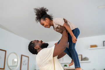 African love family moment, joyful father lifting daughter in the air, playful, happiness, laughter, affectionate parenting childhood memories, togetherness, care and father’s day celebration at home