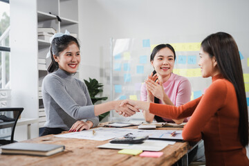 Fototapeta premium Shaking hands, Asian people, motivated businesswoman at her desk, brainstorming creative ideas to kickstart her startup venture with determination and innovation. purpose and ambition. only women.