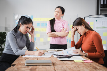 Fototapeta premium Asian people, frustrated businesswoman sits at desk, grappling with challenges of her startup, acknowledging failure, and seeking ways to learn and grow. team meeting. blamed