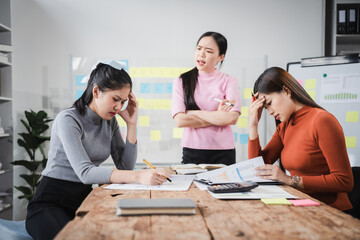 Fototapeta premium Asian people, frustrated businesswoman sits at desk, grappling with challenges of her startup, acknowledging failure, and seeking ways to learn and grow. team meeting. blamed