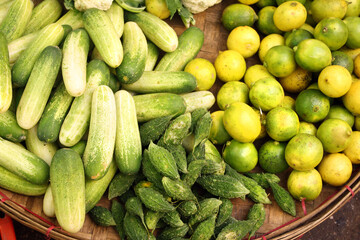 Different ripe vegetable in a wicker basket. Fresh cucumber, bitter gourd, lime for sale on street market, Southeast Asia. Fresh vegetables in a traditional morning market, Myanmar
