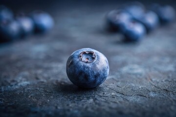 Close-up of a Single Blueberry on a Dark Surface with Blurred Background of More Berries