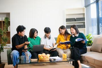 Fototapeta premium Young Asian students working on a project with laptops and tablets. Cozy indoor setting, teamwork,