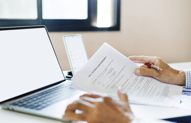 asian businessman holding personal loan agreement documents checking contract details and checking account balance via laptop to apply for loan to start new business