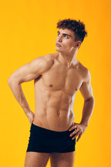 Fototapeta premium Confident young man posing in black underwear against a vibrant yellow background, showcasing fitness and healthy lifestyle. Body positivity and self-expression concept.