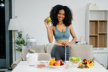 Smiling woman measuring waist, holding green apple with fruits, veggies,