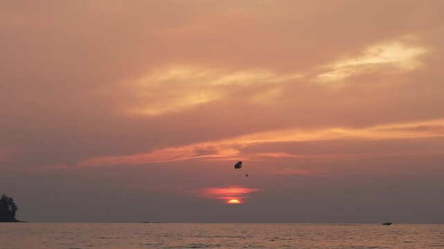 Parasailing experience at dusk showcases the beauty of the sunset over the ocean. Spectators watch as the parasailer glides through the vibrant sky.