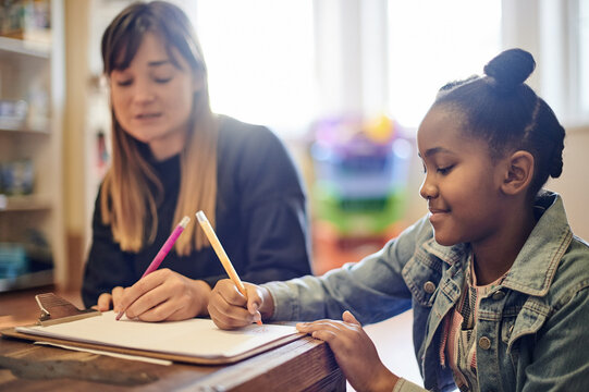 Learning, adoption and mother with black girl writing in home for homework, drawing and homeschool. Development, studying and mama helping foster kid, student or child with education on clipboard. - Powered by Adobe