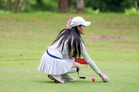  Asian woman happy and fun while playing golf on the golf course. Golfer hitting golf shot with driver club on course. Beautiful woman smiling and holding a golf club while standing on green lawn.