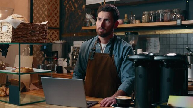 Pensive Caucasian staff employee restaurant worker barista guy using laptop ordering products online shopping in Internet male small business owner thinking in cafeteria waiter man type computer cafe