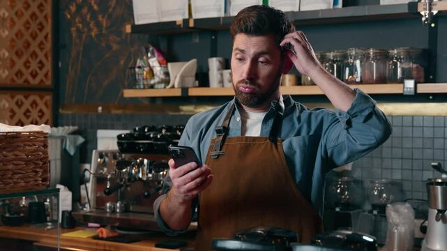 Frustrated stressed Caucasian bartender holding mobile phone fail bankruptcy man barista male waiter cafe trouble guy restaurant staff upset worker small business owner reading bad news in cafeteria